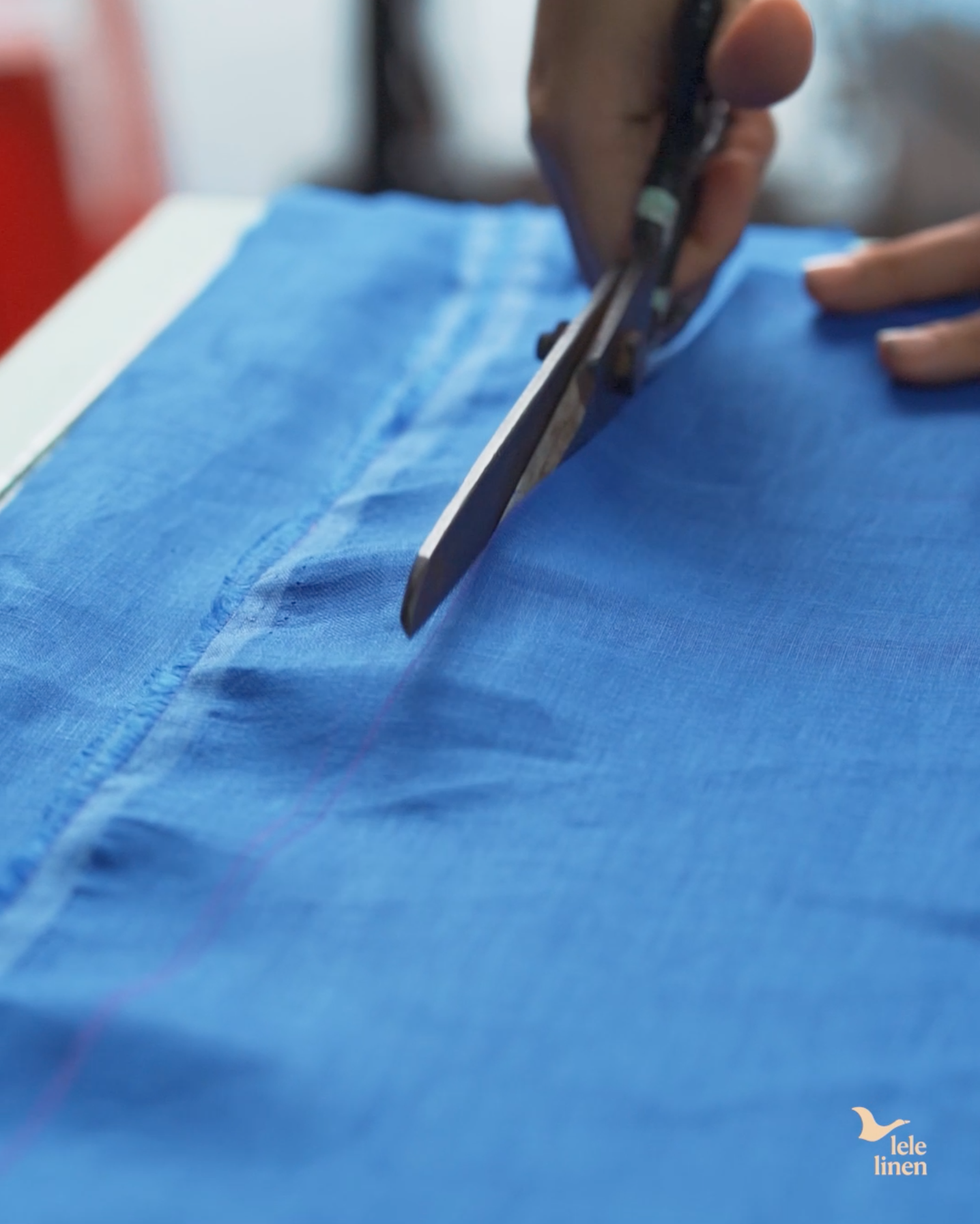 Cutting blue linen fabric with tailoring scissors along a marked line
