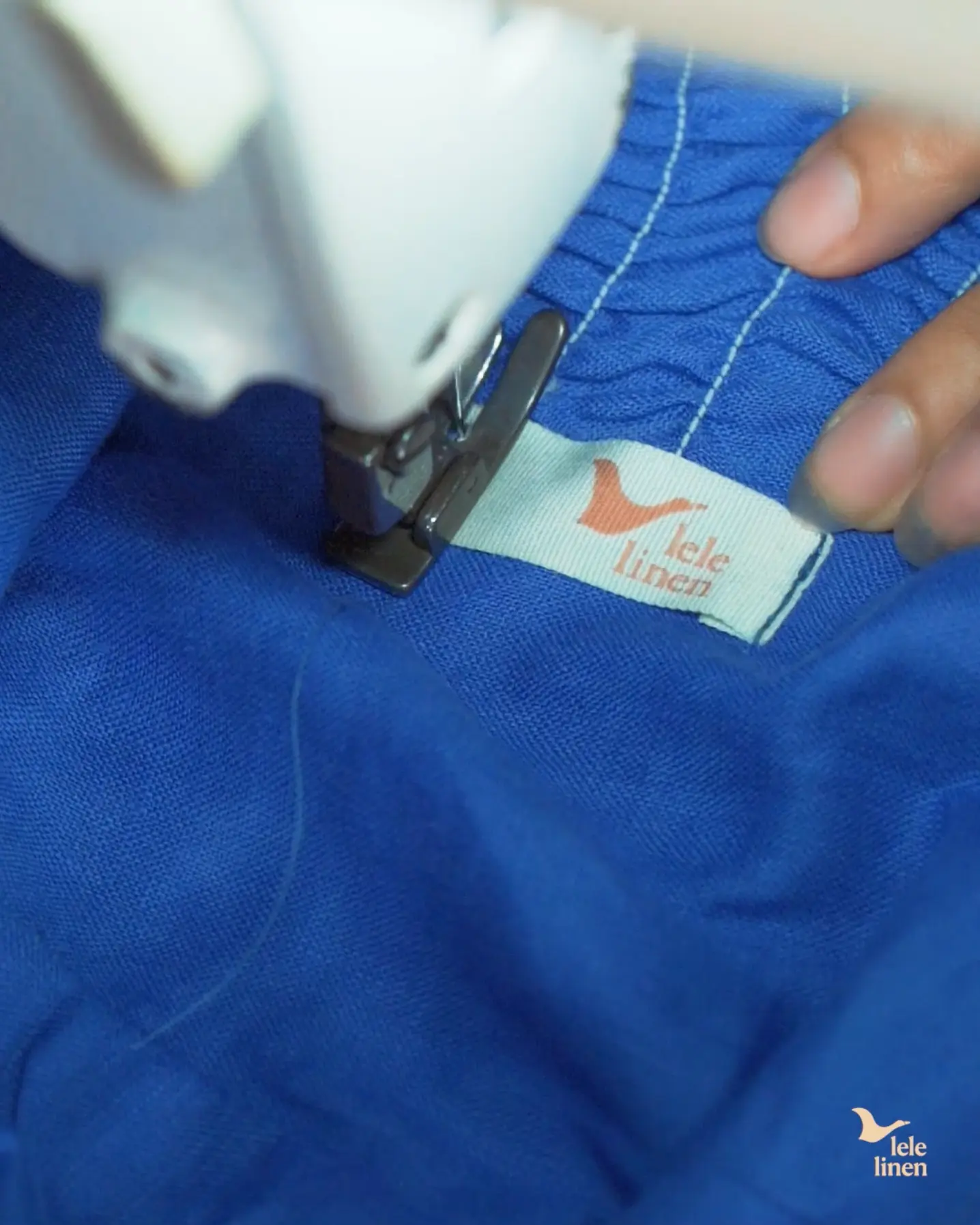 Sewing a Lele Linen label onto a blue linen garment at the machine