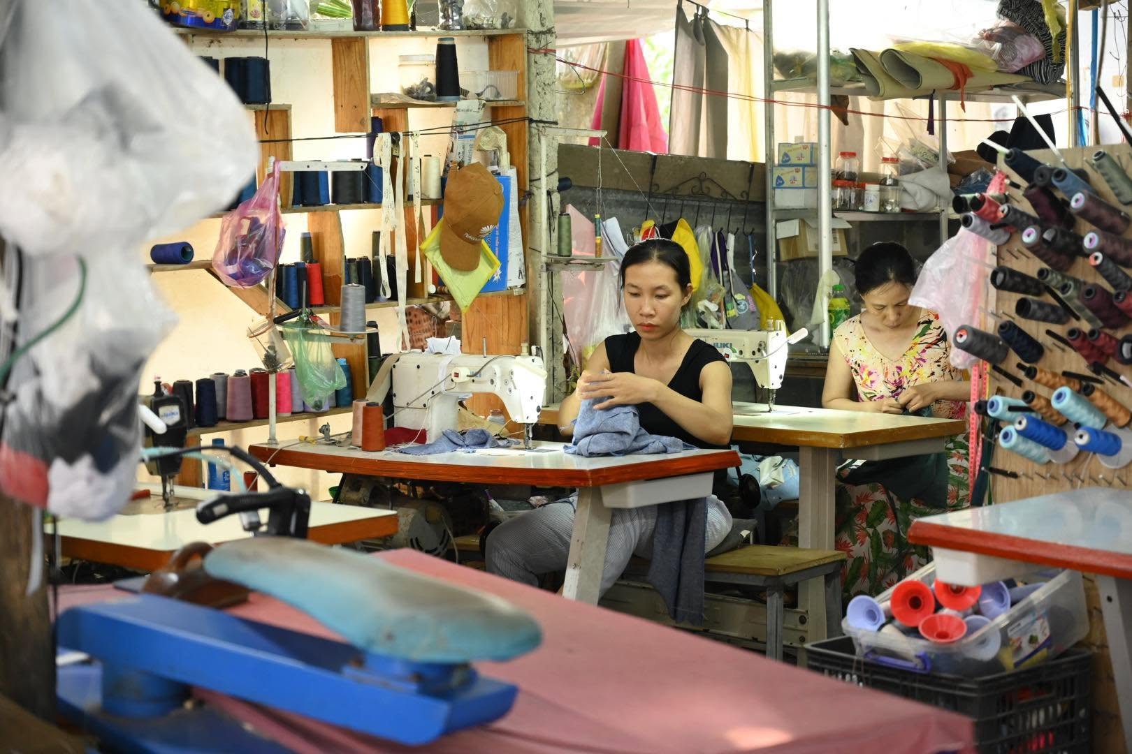 Two tailors sewing at their machines inside the Lele Linen workshop surrounded by thread spools.