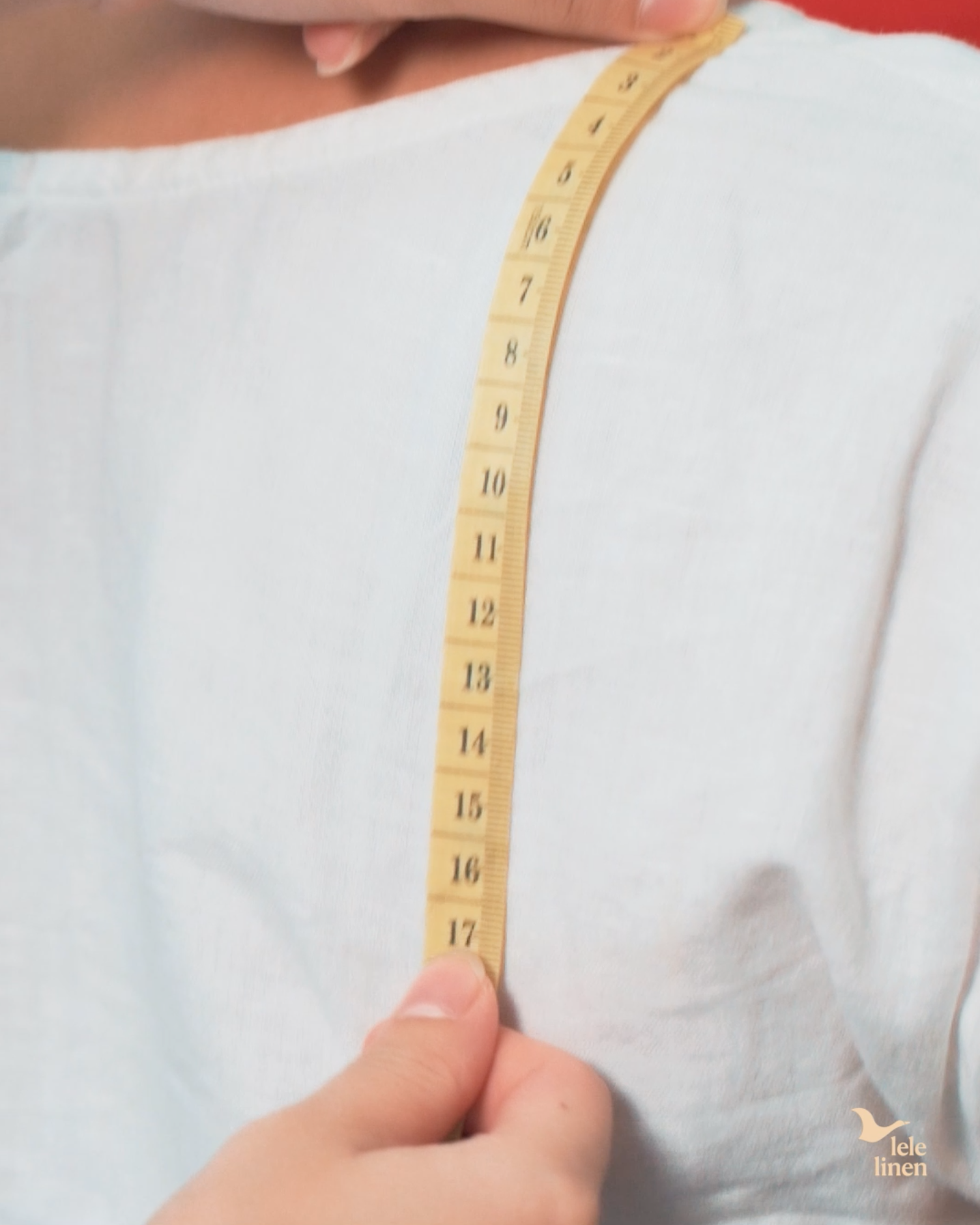 Taking a shoulder measurement over a white linen top in the Lele Linen studio